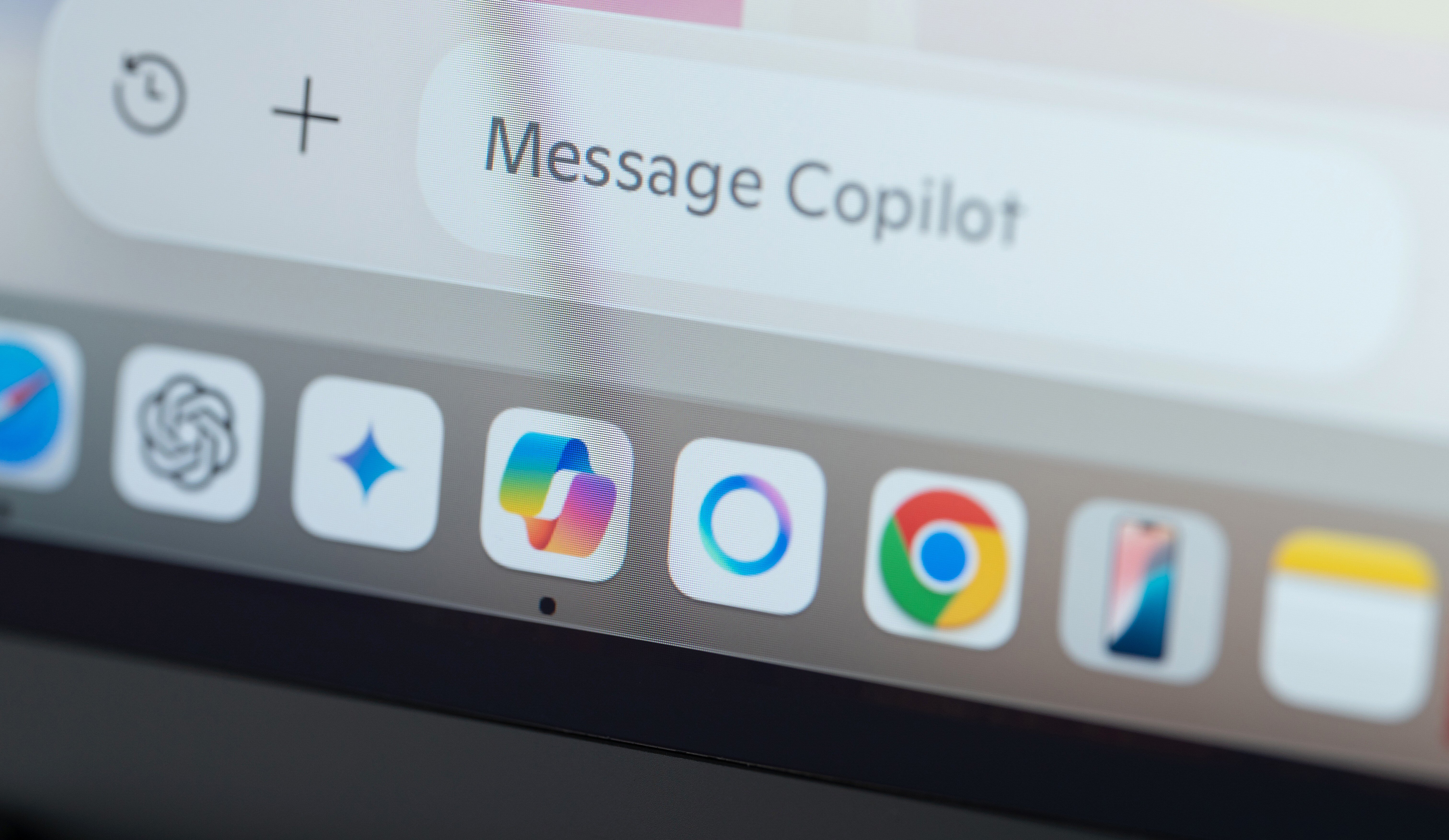 Close-up of a computer screen showing a dock with various app icons including Safari, ChatGPT, Microsoft Copilot, Google Chrome, and others, with a search bar displaying 'Message Copilot'.