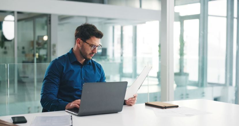 Laptop, reading and documents with business man in office for research, payroll manager and audit report. Planning, budget review and accounting firm with person in agency for tax benefit and email