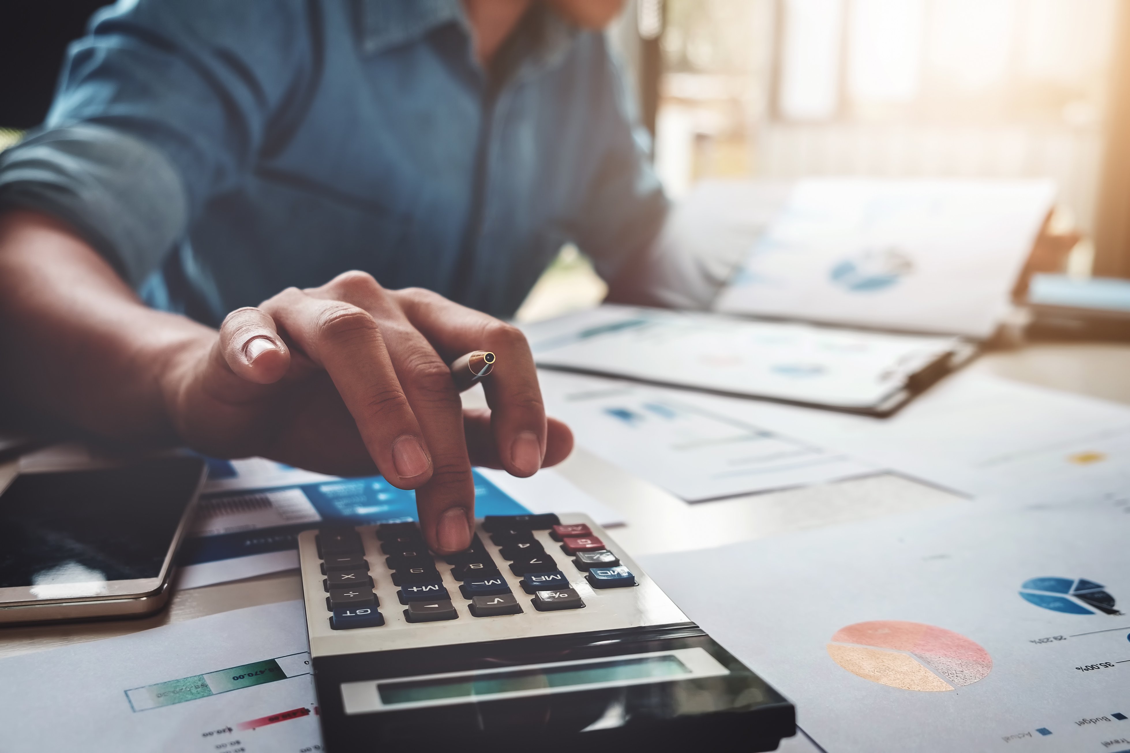 Man using calculator with computer laptop, budget, and loan paper in office.