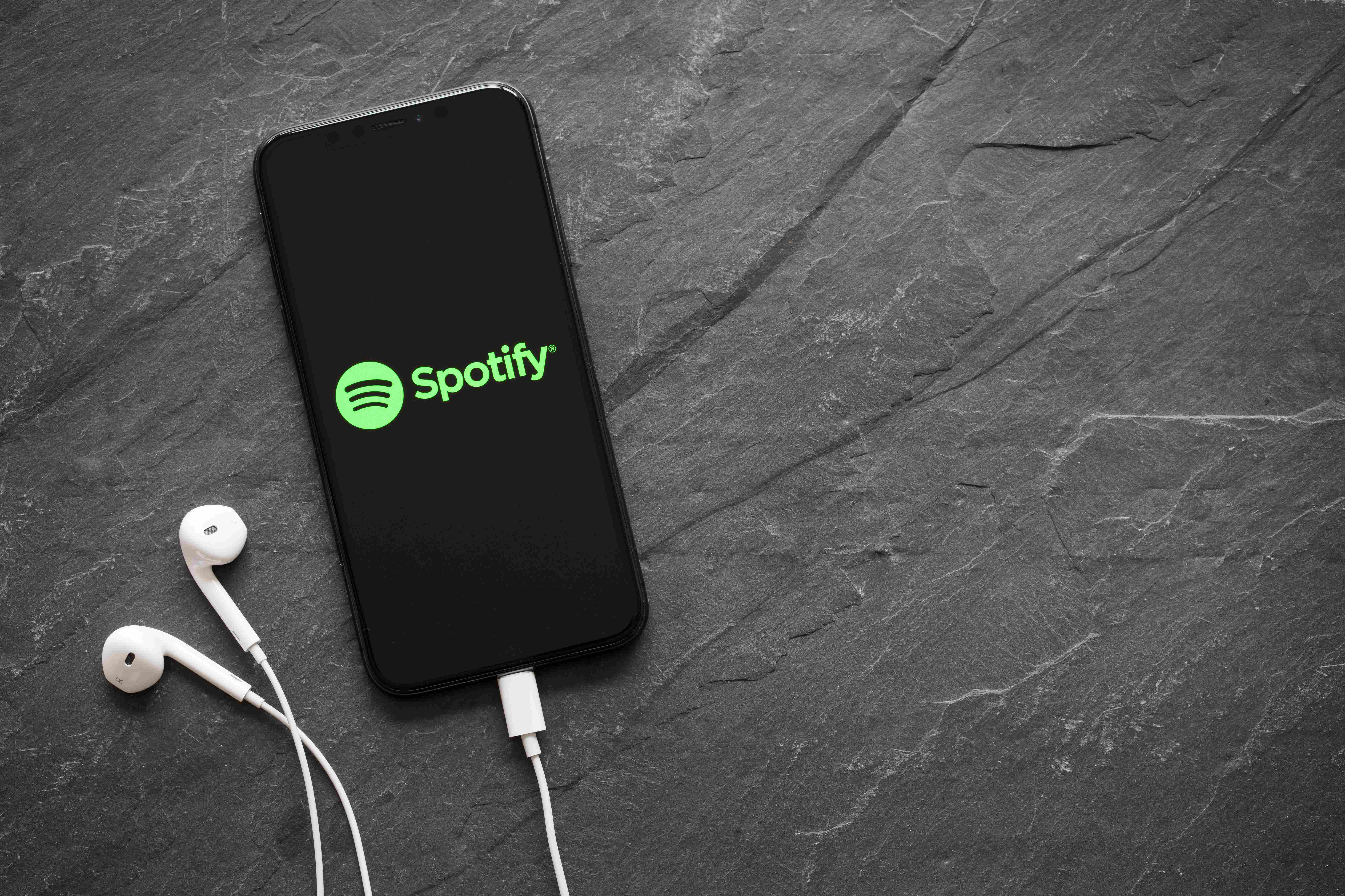 Mobile Phone on grey background, the screen shows the Spotify logo and has a pair of headphones attached 