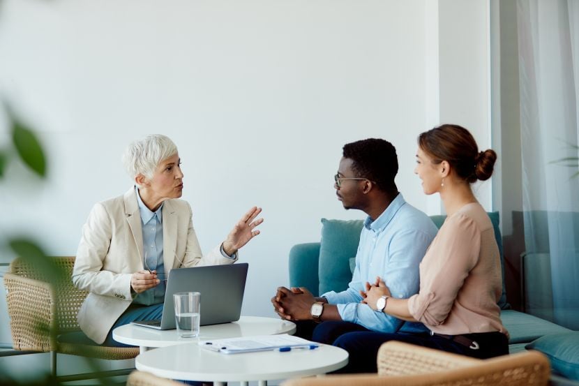 Mature financial adviser using laptop while has consultations with multiracial couple in the office.
