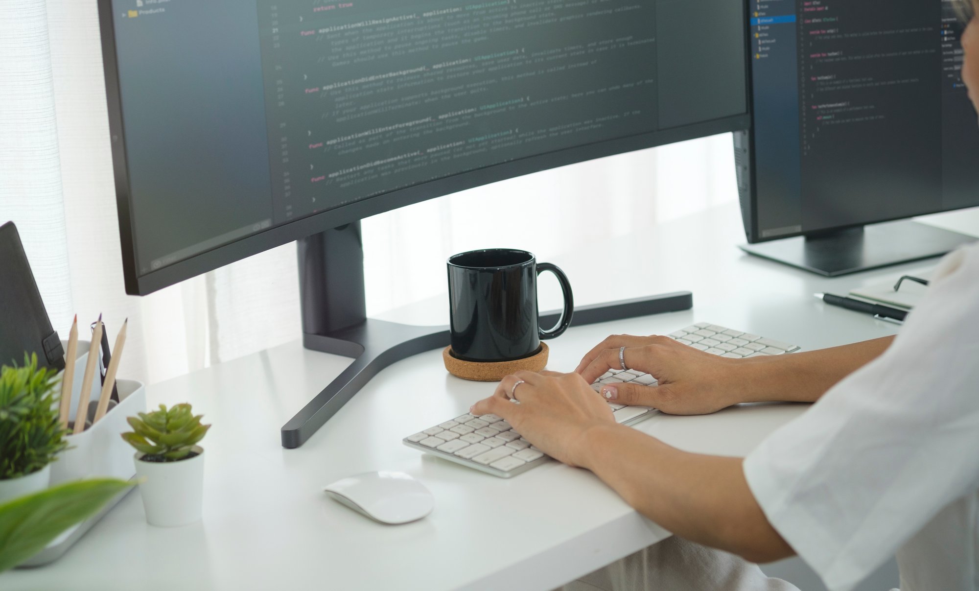 Cropped shot of young programmer writing program code with two monitors in bright office