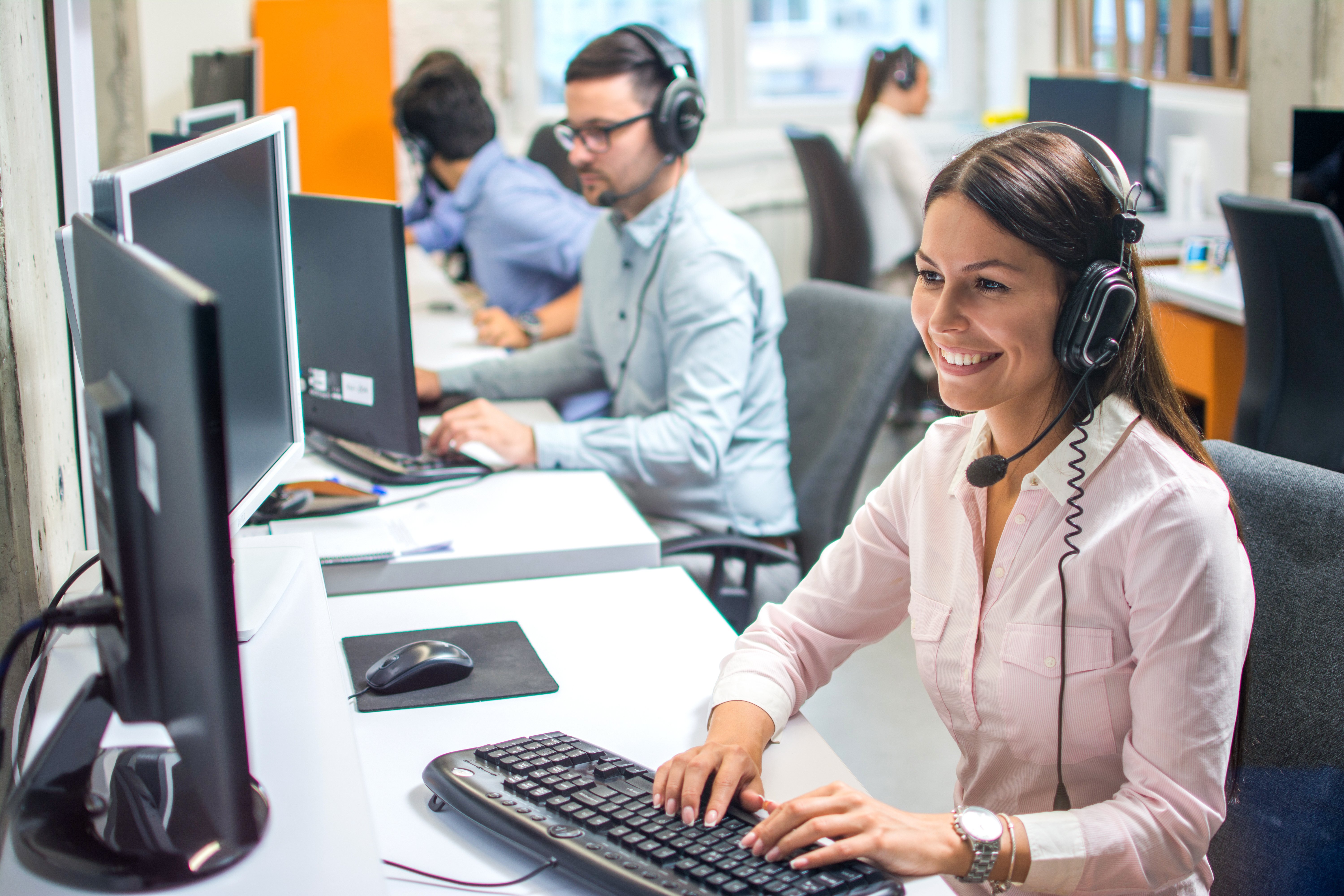 Row of customer support agents working on computer in office. Helpdesk, online support services, telephone workers and sales agents concept.