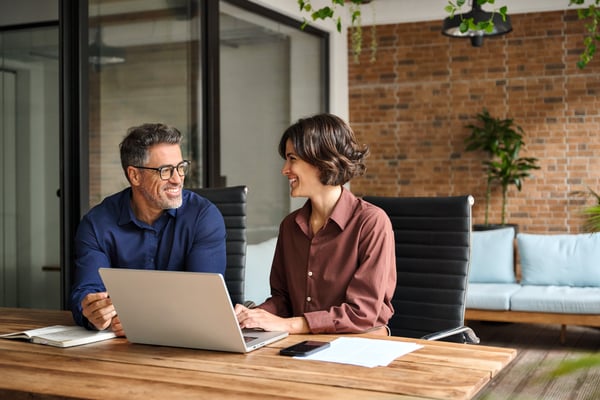 A man and a woman discussing SharePoint at a wooden desk.