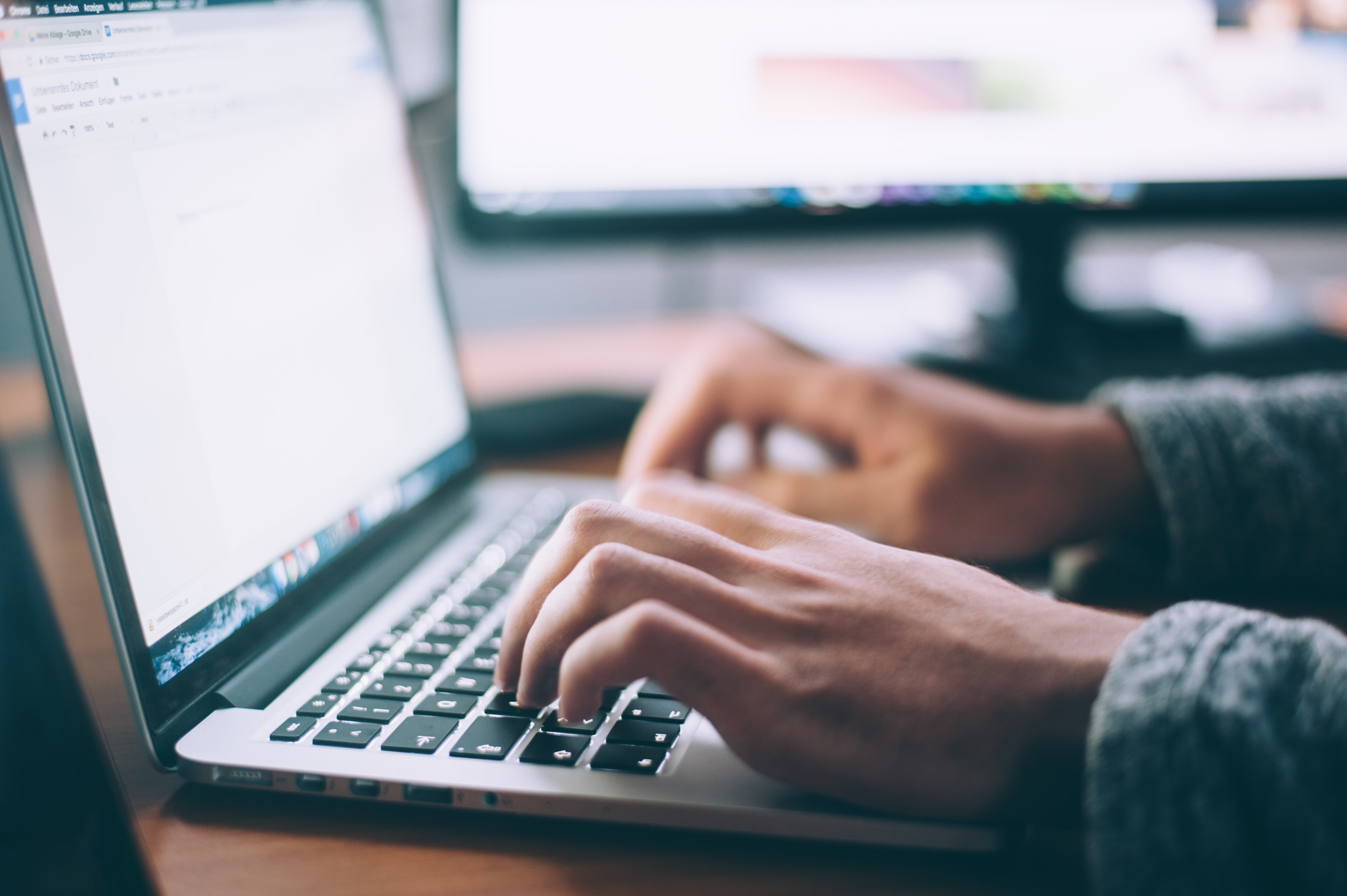 Typing at a laptop and monitor.