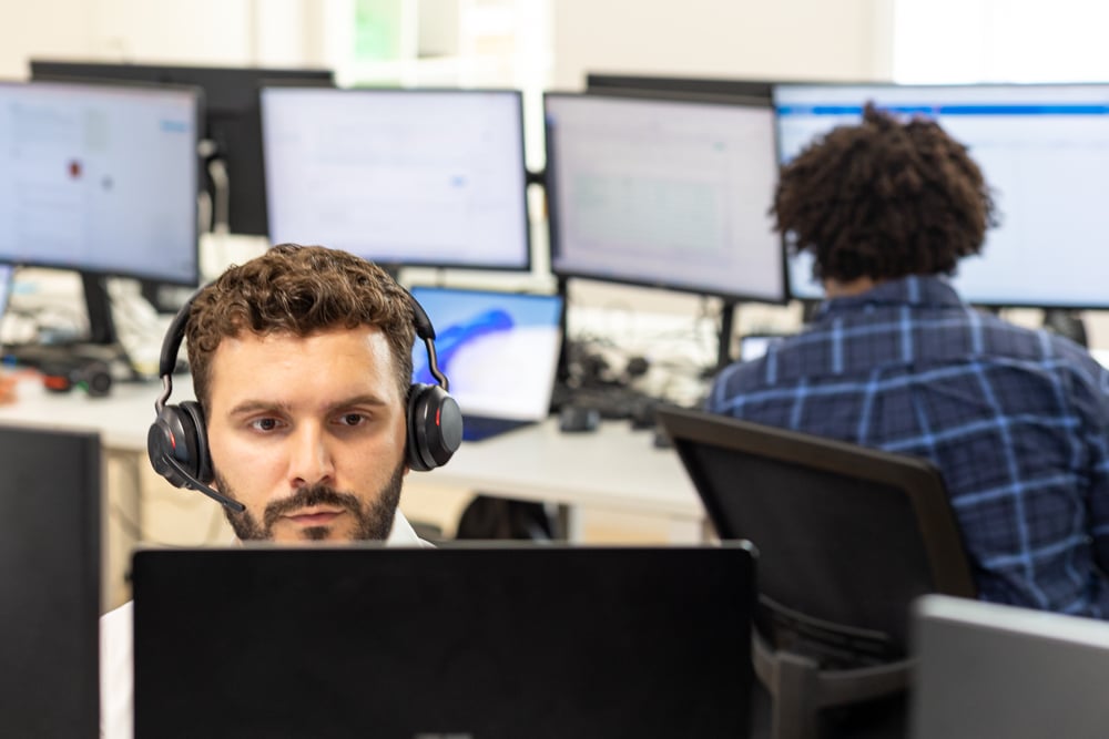 Fitzrovia IT managed IT support engineer wearing a headset while assisting a client from a multi-monitor workstation